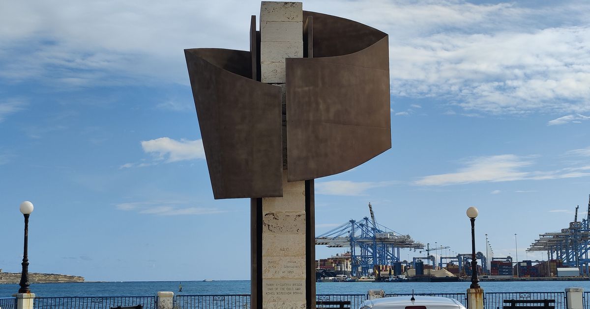Monument magħmul mill-metall u l-ġebla. Ħdejn il-baħar, bil-krejnijiet faċċata.